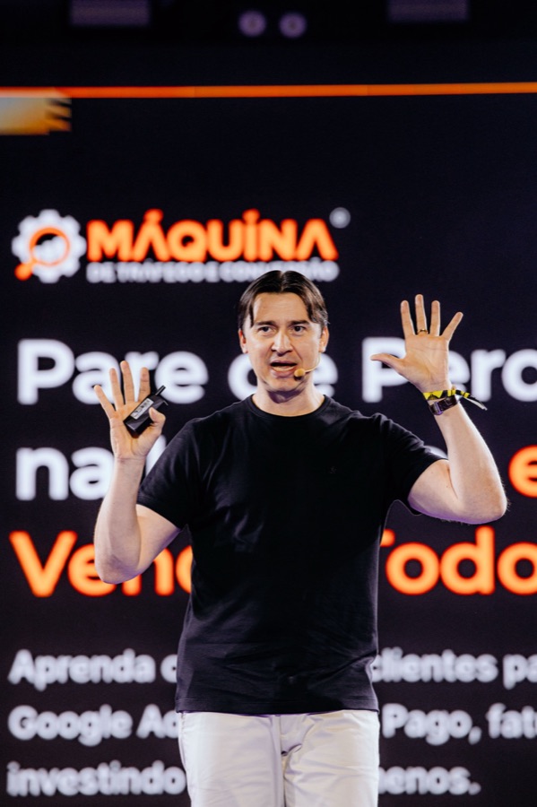 Adriano Gianini palestrando no RD Summit 2024, com a marca do Máquina de Tráfego e Conversão no telão